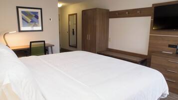 A hotel room with a large bed, a desk with a chair, a wardrobe, a television, and a framed picture on the wall.