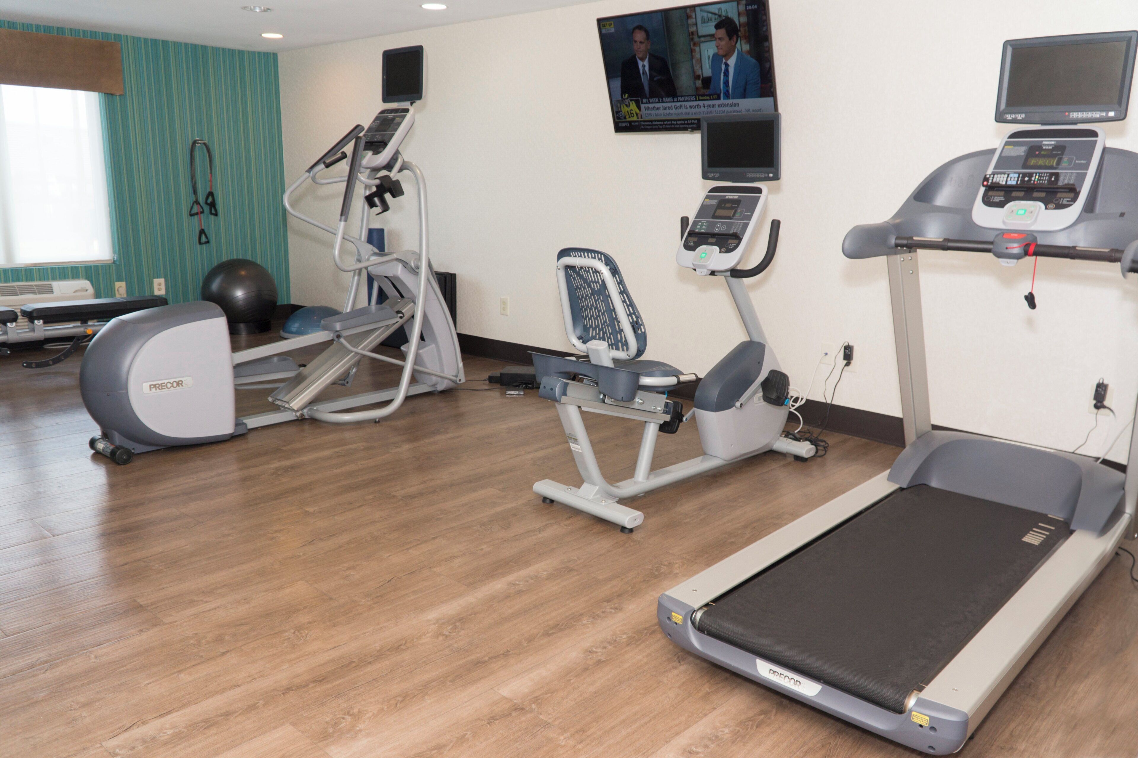 Un centre de remise en forme équipé de machines de cardio, d’un téléviseur fixé au mur et de ballons d’exercice.