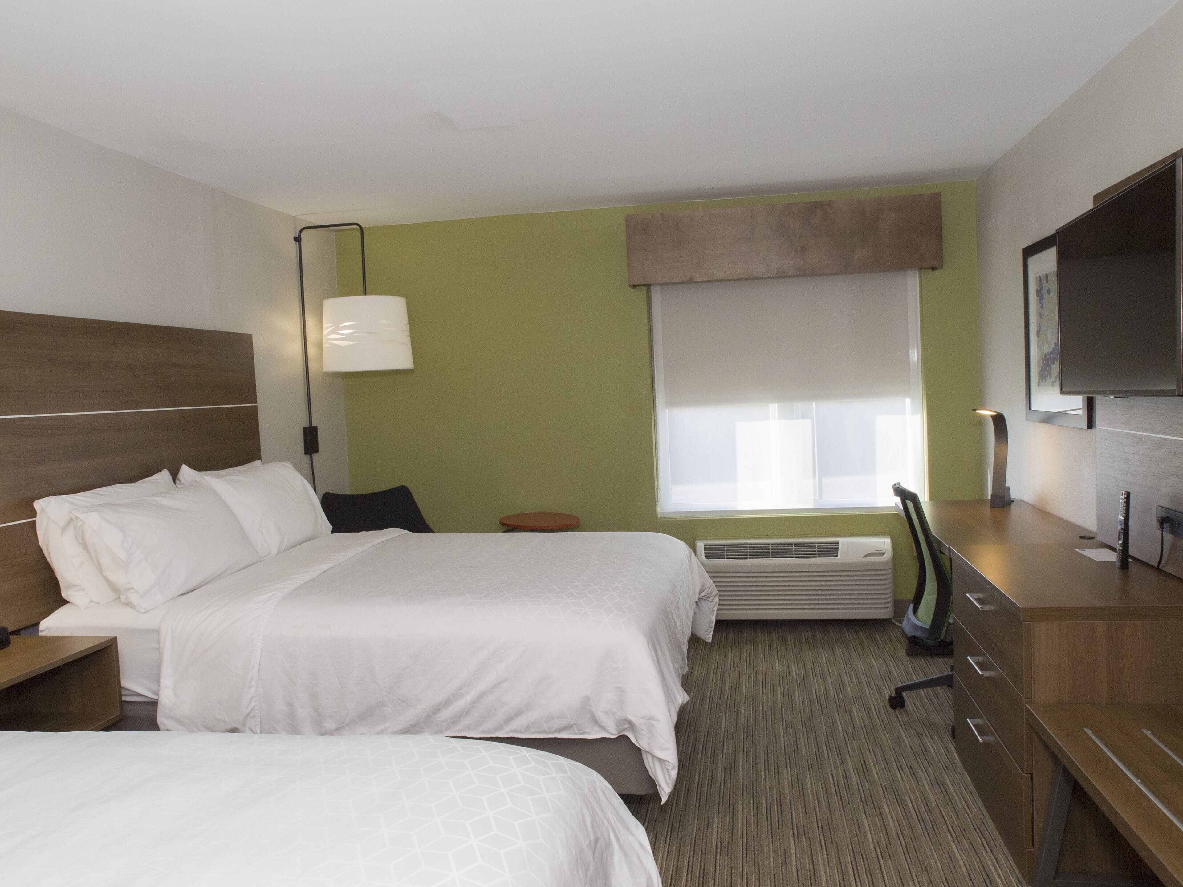 Une chambre d’hôtel avec deux lits, un bureau, une chaise, une télévision et une fenêtre avec des stores.