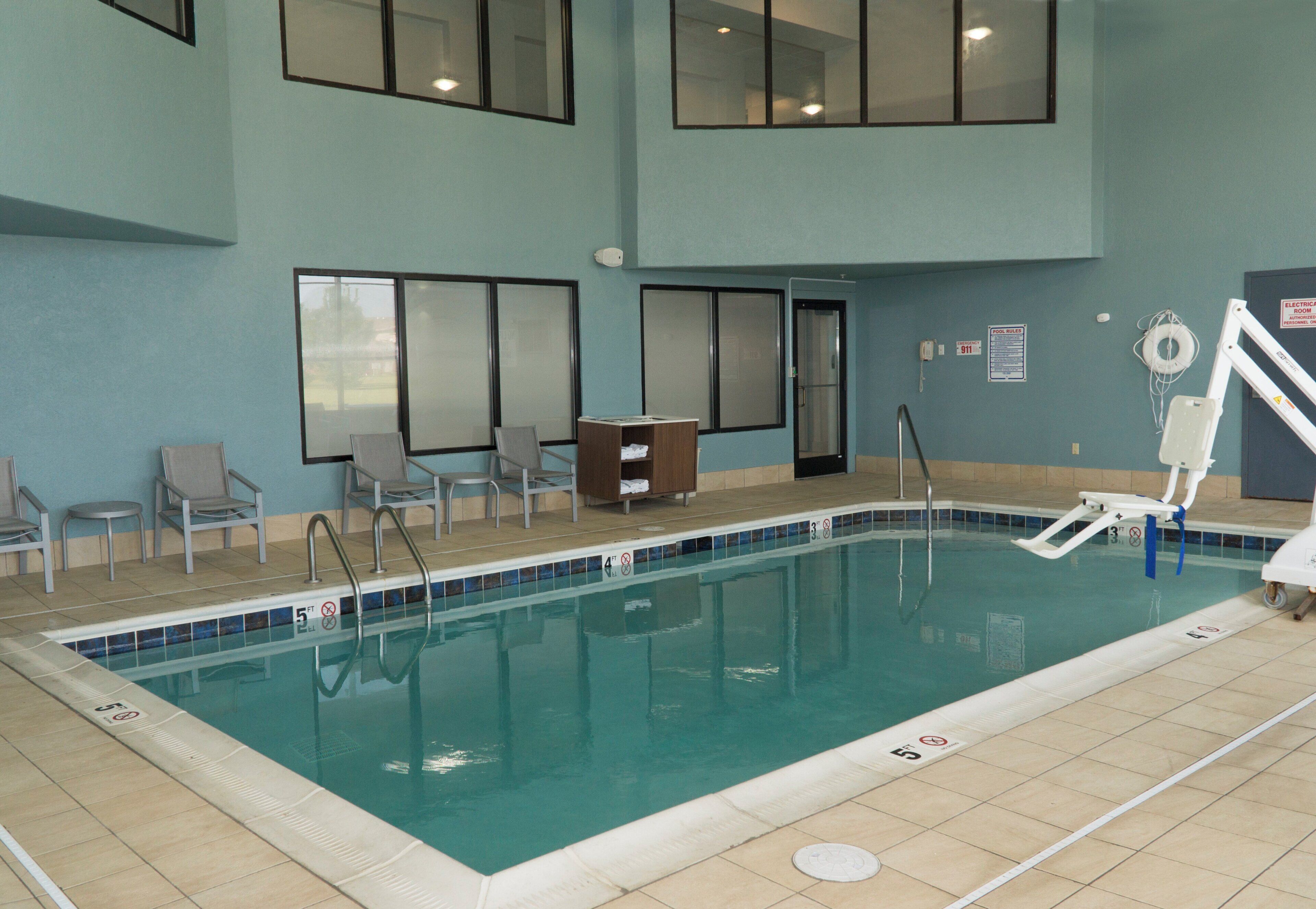 Piscina interior con agua cristalina, rodeada por una terraza con baldosas. Hay sillones de descanso y una pequeña mesa cerca de la piscina.