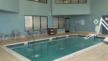 Piscina interior con agua cristalina, rodeada por una terraza con baldosas. Hay sillones de descanso y una pequeña mesa cerca de la piscina.