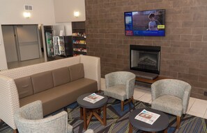 A hotel lobby with a brown sofa, two armchairs, a fireplace, a television, and a refrigerator. - Holiday Inn Express Hotel & Suites Madison by IHG (Madison)