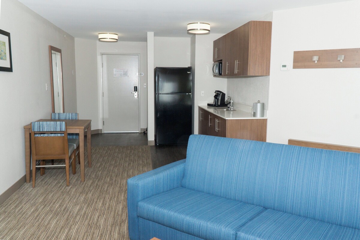 A compact hotel room with a kitchenette, a dining area with a table and chairs, and a sofa.