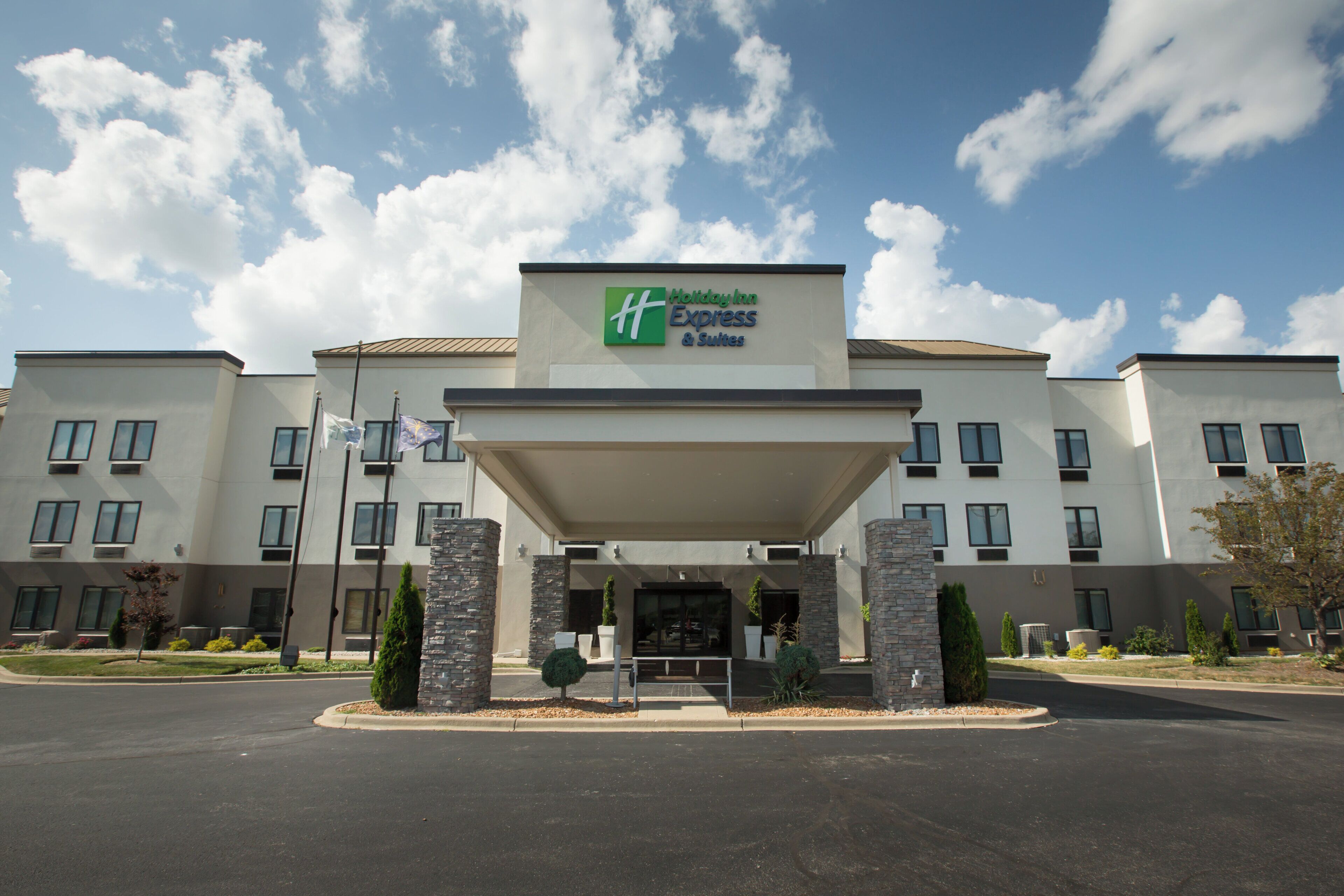 Un hotel Holiday Inn Express & Suites con un diseño arquitectónico moderno, que presenta una entrada cubierta y un jardín frontal ajardinado.