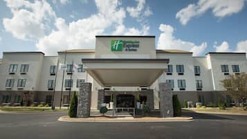 Un hotel Holiday Inn Express & Suites con un diseño arquitectónico moderno, que presenta una entrada cubierta y un jardín frontal ajardinado.