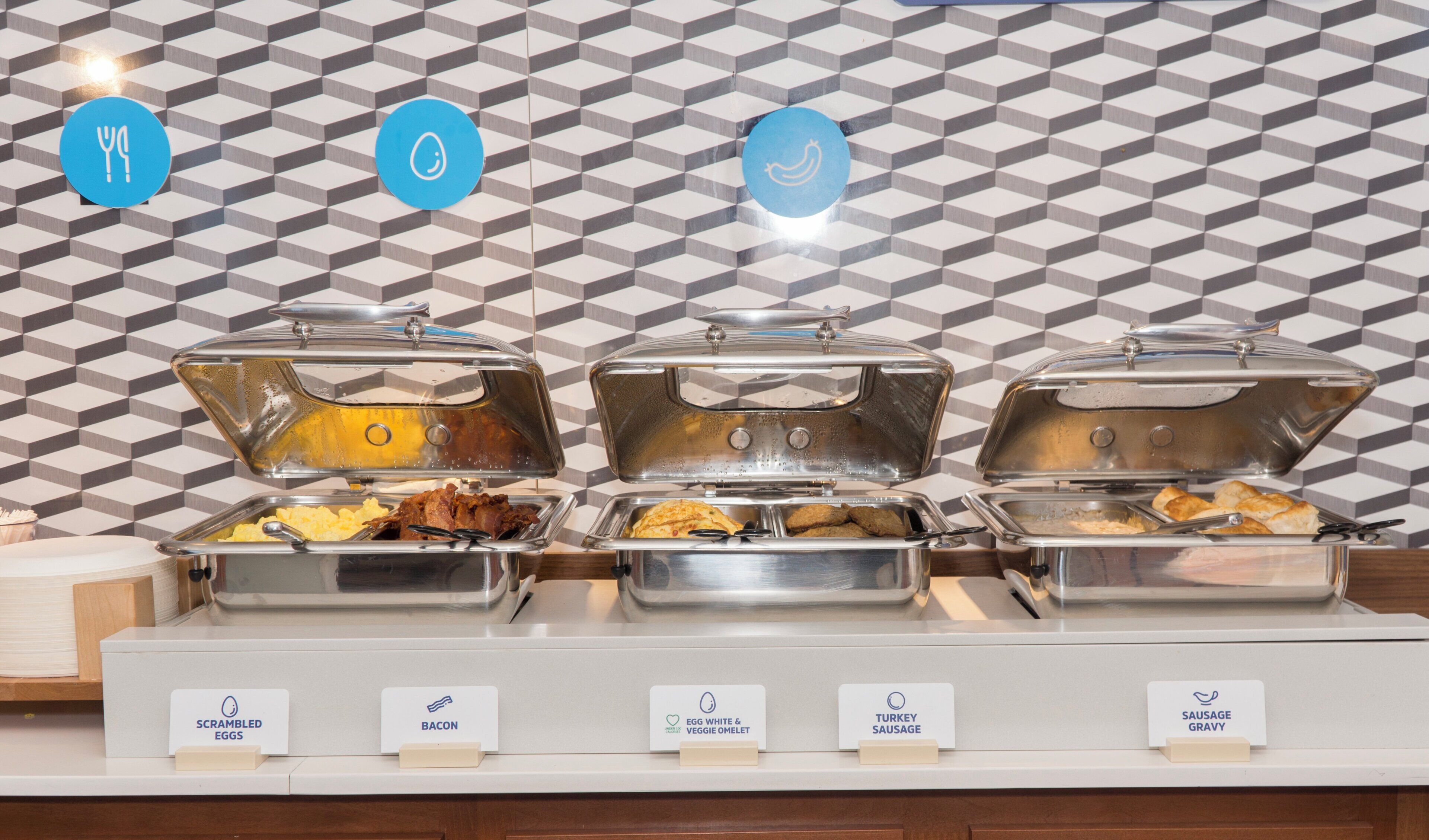 A buffet with labeled containers for scrambled eggs, bacon, egg white & veggie omelet, turkey sausage, and sausage gravy.
