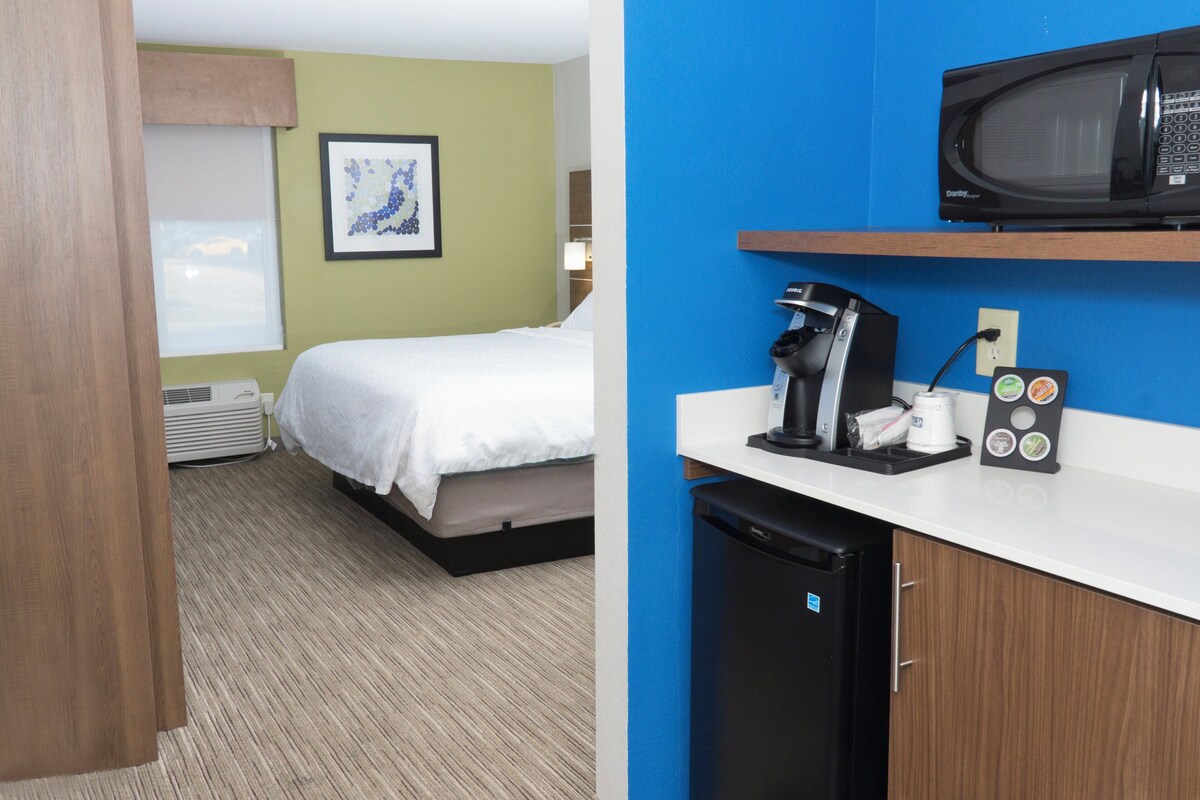 Habitación de hotel con cama, kitchenette pequeña, microondas y cafetera.