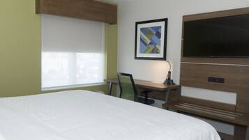 A hotel room with a large bed, a desk with a chair, a television, and a framed picture on the wall.