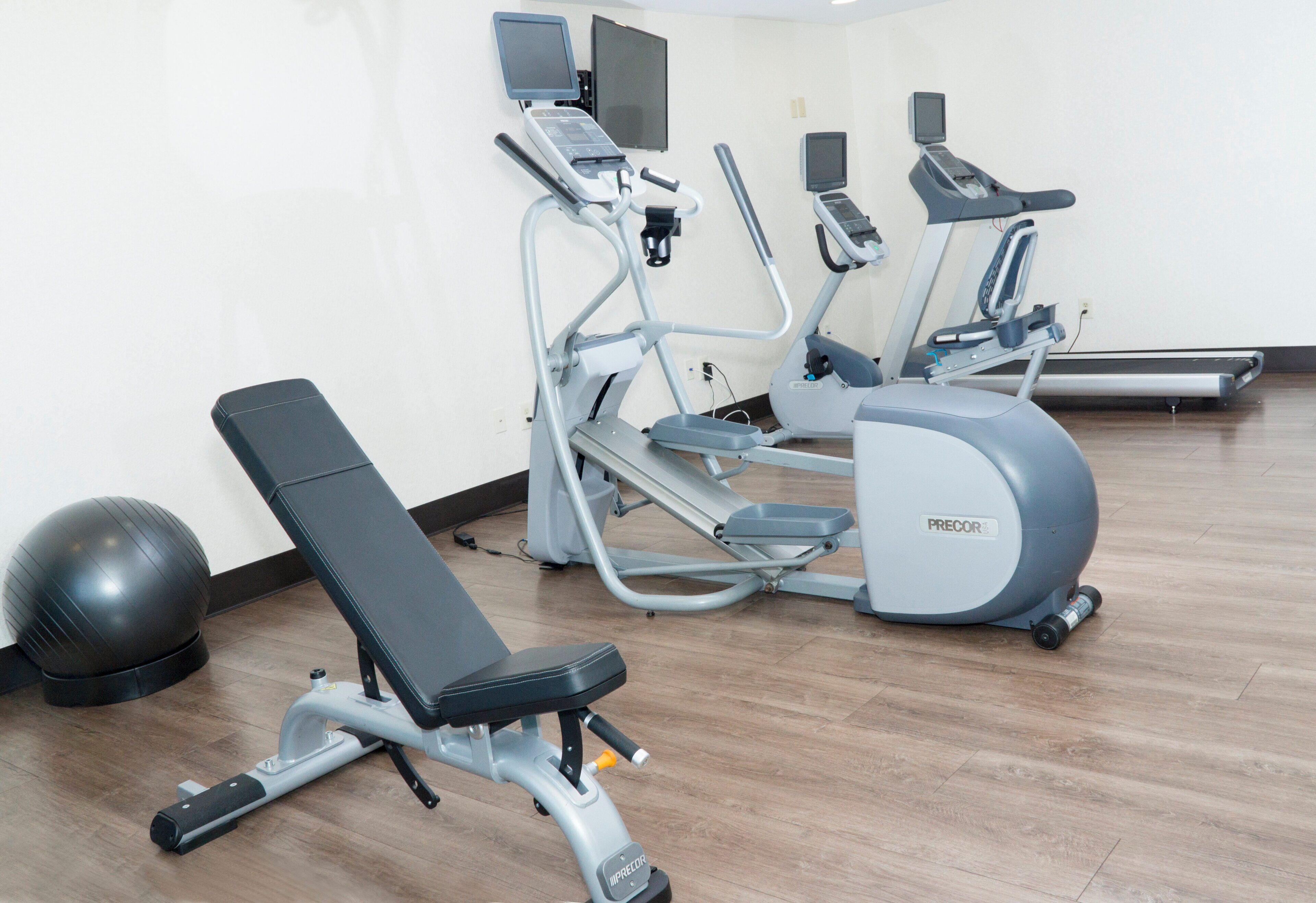 Un gimnasio con equipo de ejercicios, incluyendo una banca, elípticas y una bicicleta estática.