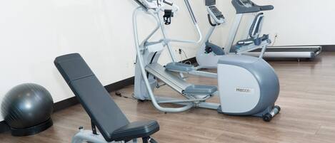 Un gimnasio con equipo de ejercicios, incluyendo una banca, elípticas y una bicicleta estática.