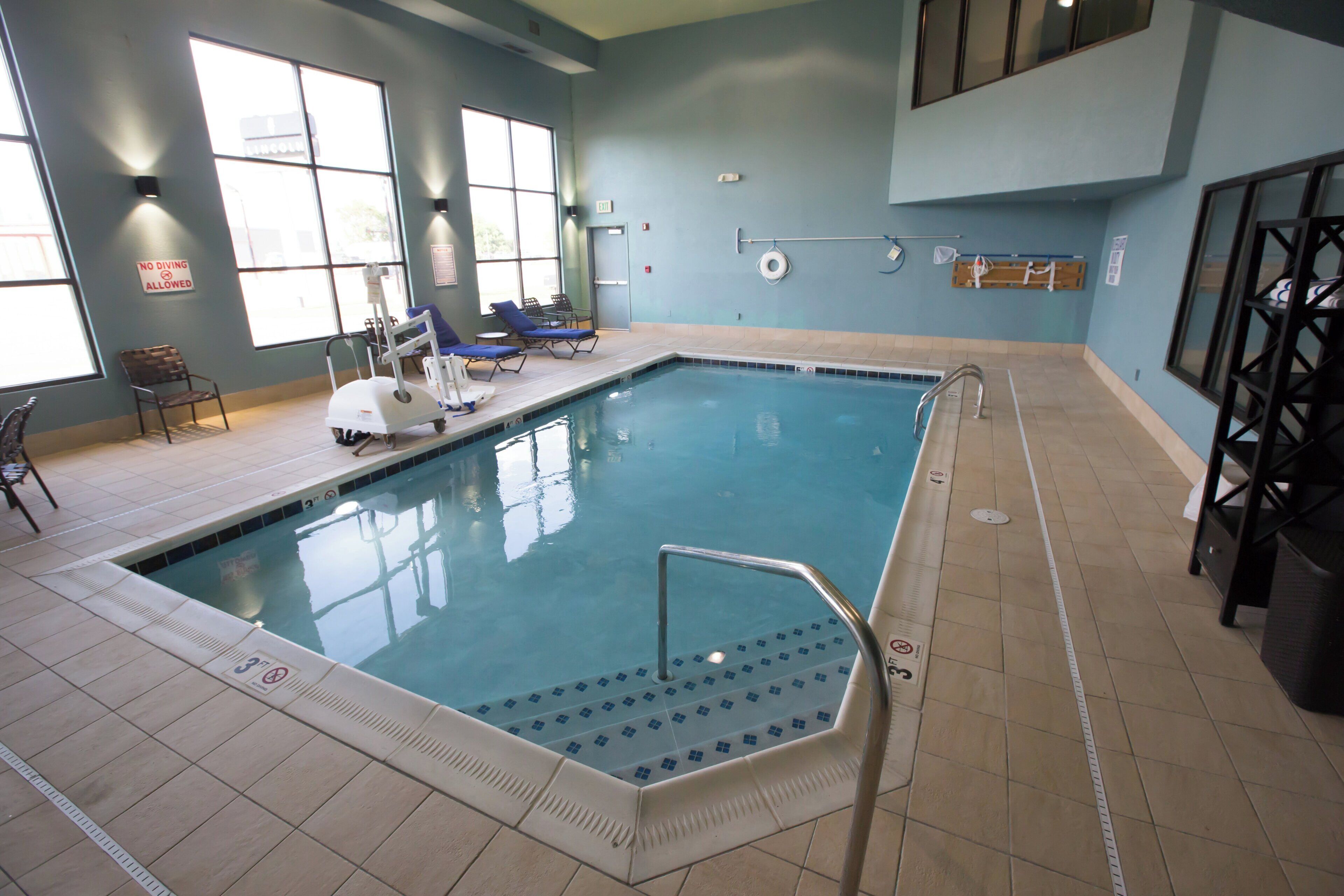 An indoor swimming pool with clear water, a diving board, and lounge chairs.