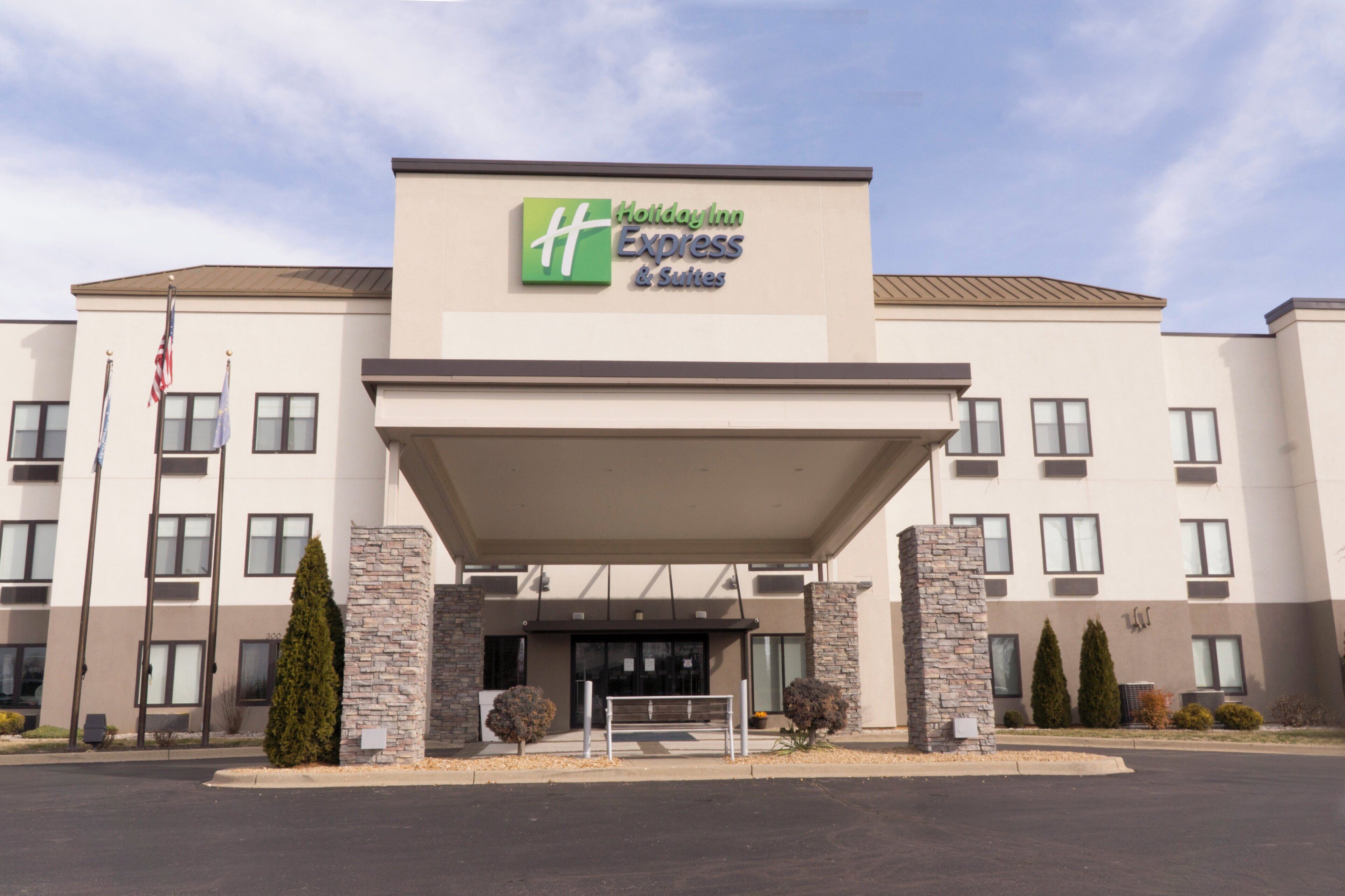 Un hotel Holiday Inn Express & Suites con fachada moderna, pilares de piedra y cielo despejado.