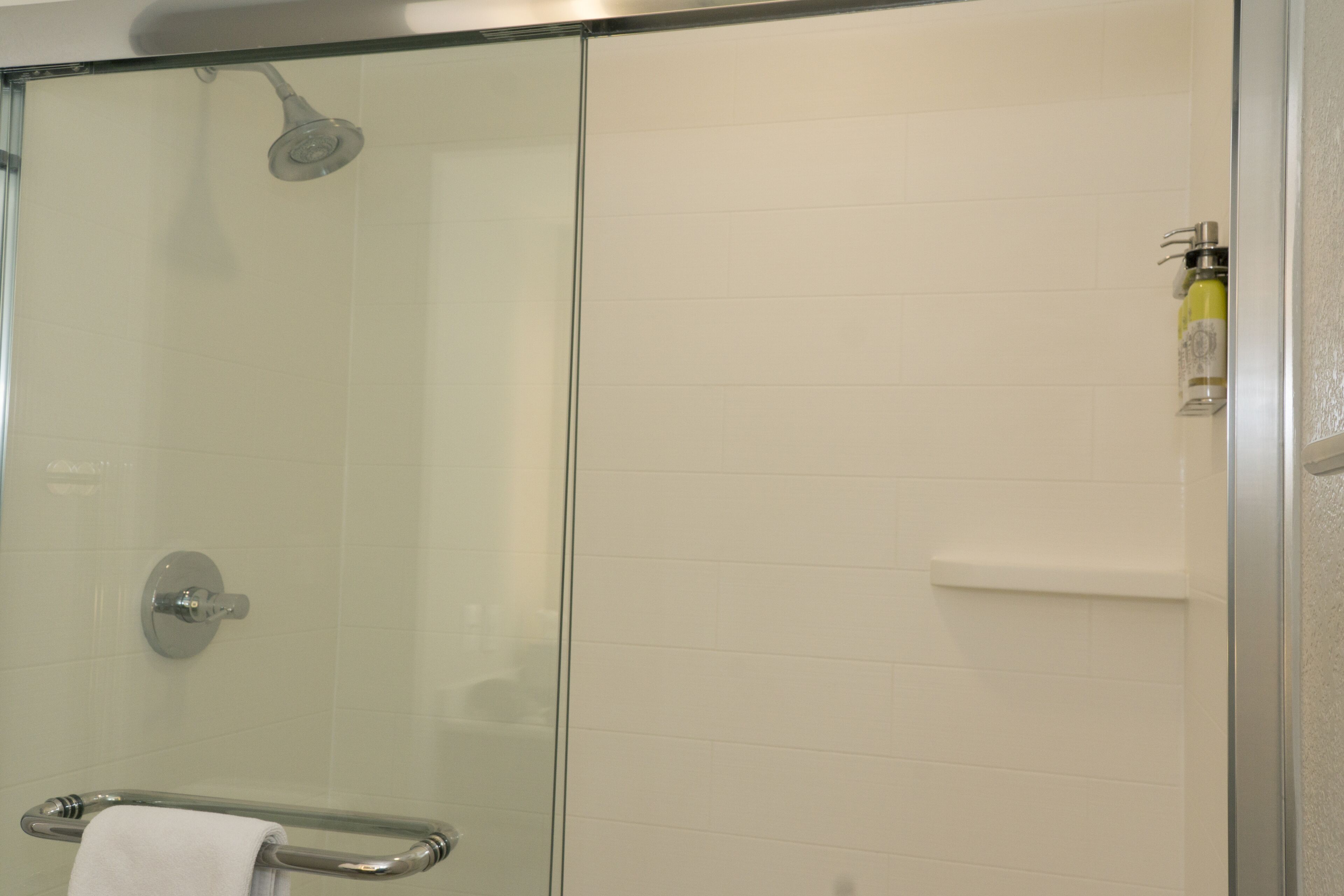 A glass-enclosed shower with a handheld showerhead, a glass door, and a towel rack with a white towel.