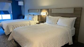 Habitación de hotel con dos camas, cabecero de madera, mesita de noche y ventana con persianas.