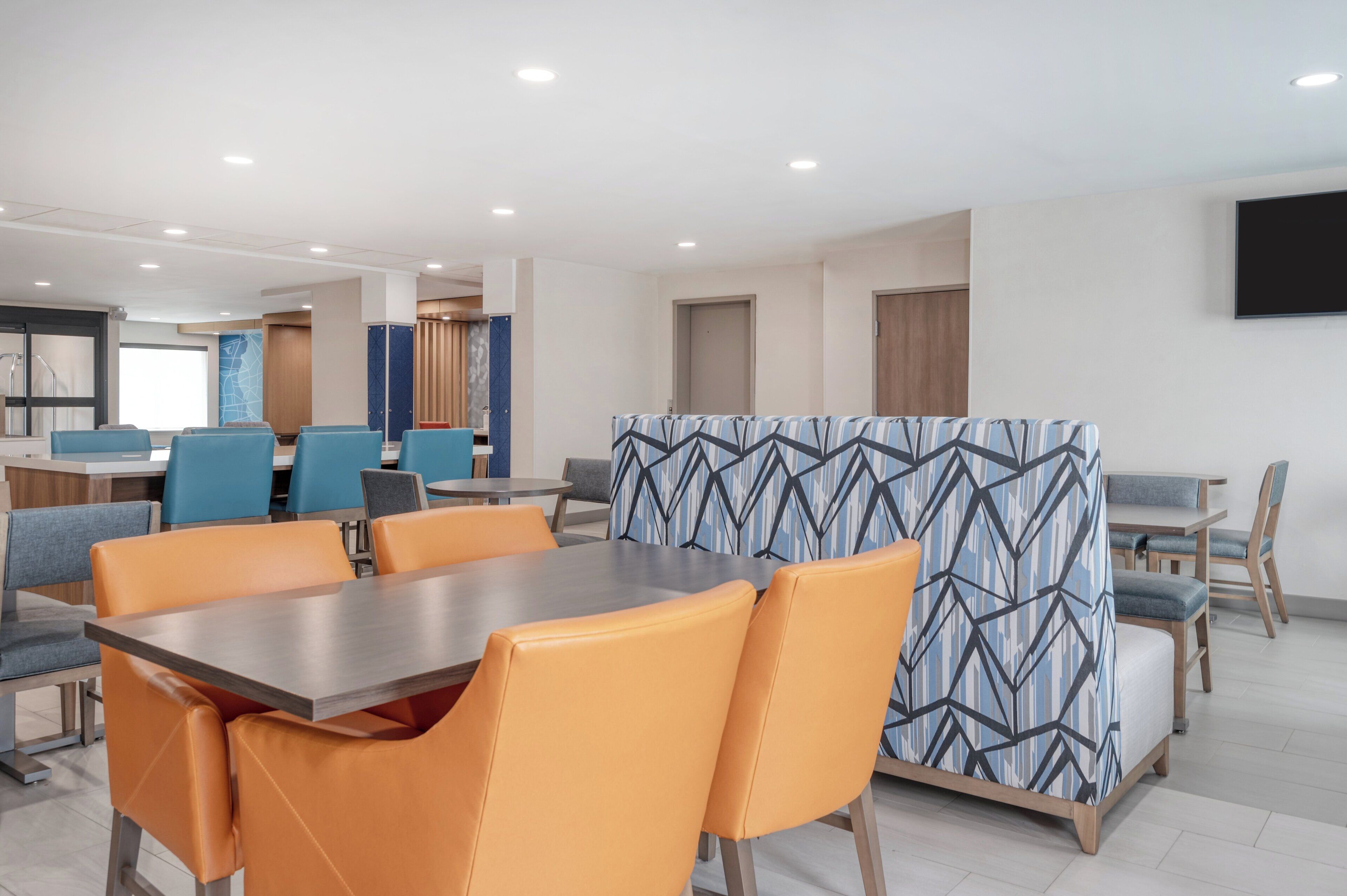 A modern dining area with a long table, orange chairs, and a patterned partition.