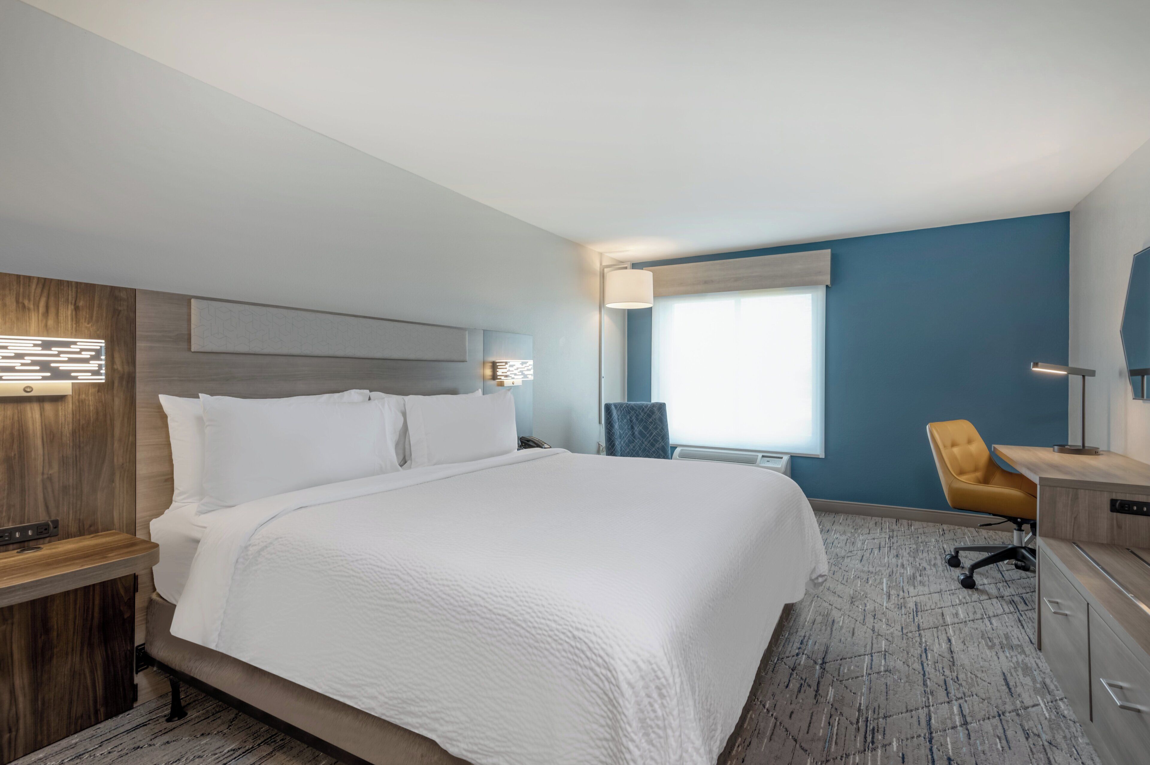 A hotel room with a large bed, a desk, a chair, and a window.