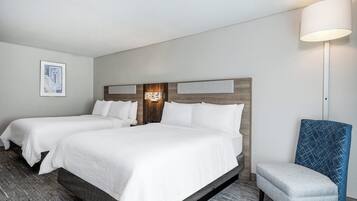 A hotel room with two beds, a nightstand, a lamp, and a chair.