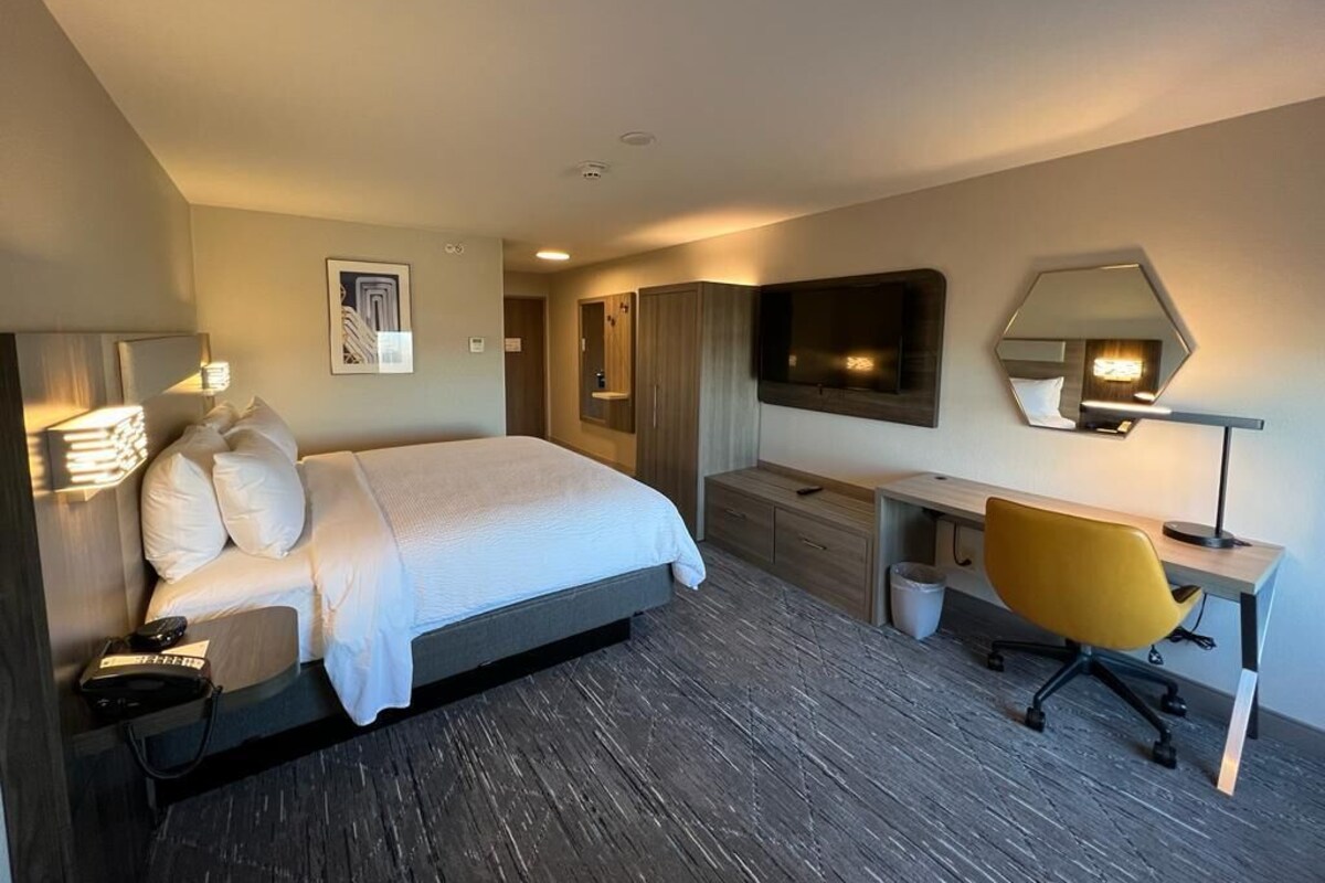 A hotel room with a bed, a desk, a chair, a TV, and a mirror.