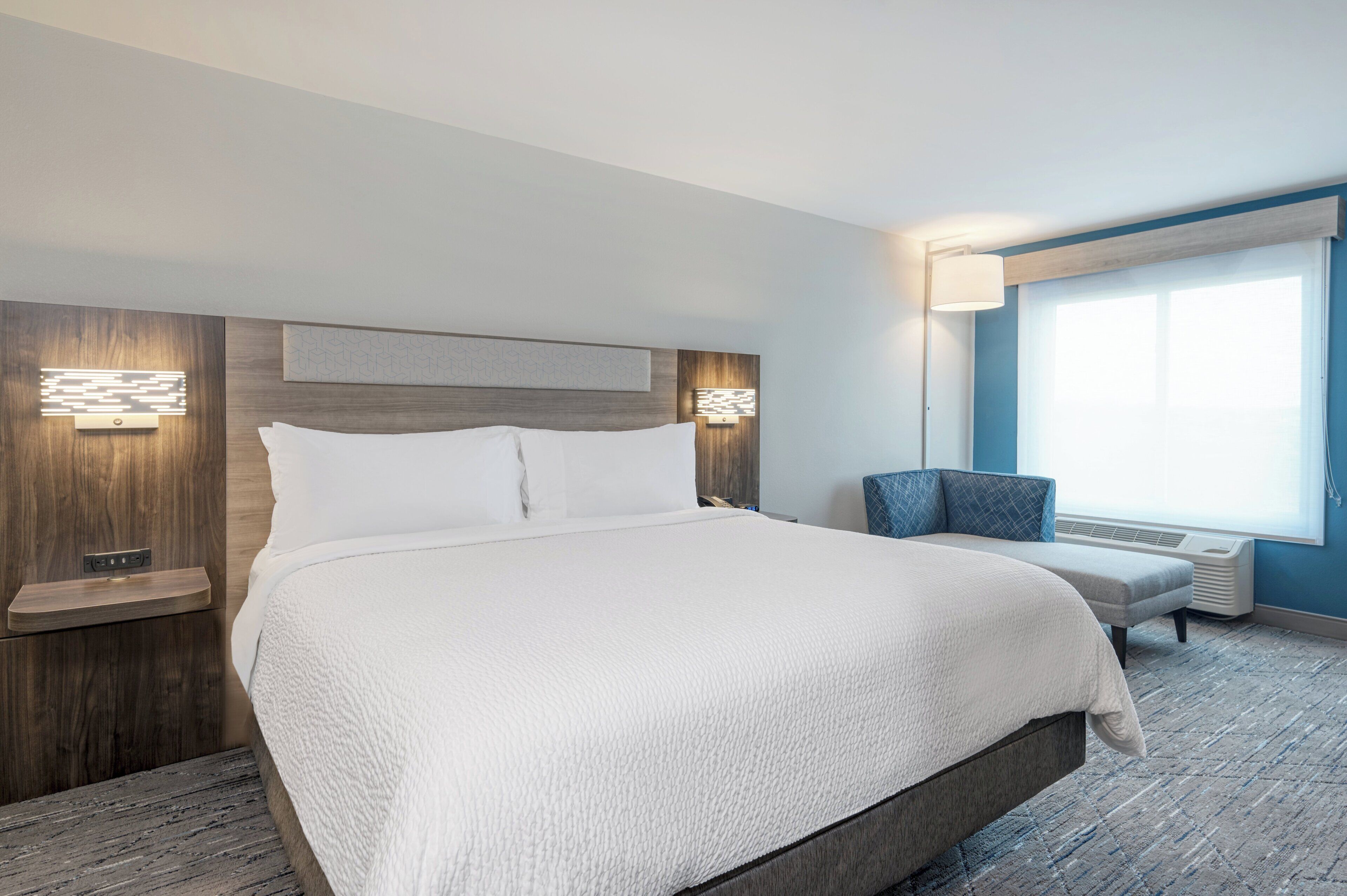 Ein Hotelzimmer mit einem großen Bett, einem Sessel, einem Schreibtisch und einem Fenster.