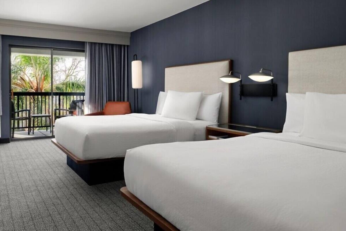 A hotel room with two beds, a balcony with a view, and a desk with a lamp.