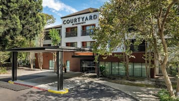 A Courtyard by Marriott hotel entrance with a covered walkway, trees, and a clear sky.