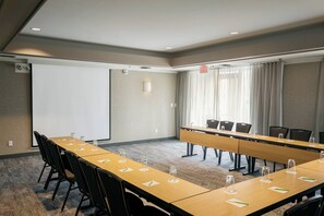A conference room with a long table, chairs, a projector screen, and a large window with curtains. - Courtyard by Marriott Stockton (Stockton)