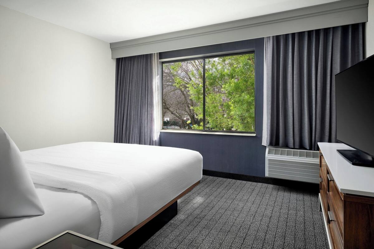 A hotel room with a bed, a desk, a TV, and a window with curtains.