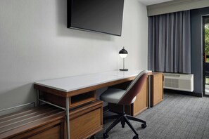 A hotel room with a wooden desk, a chair, a flat-screen TV mounted on the wall, a desk lamp, and a large window with curtains. - Courtyard by Marriott Stockton (Stockton)