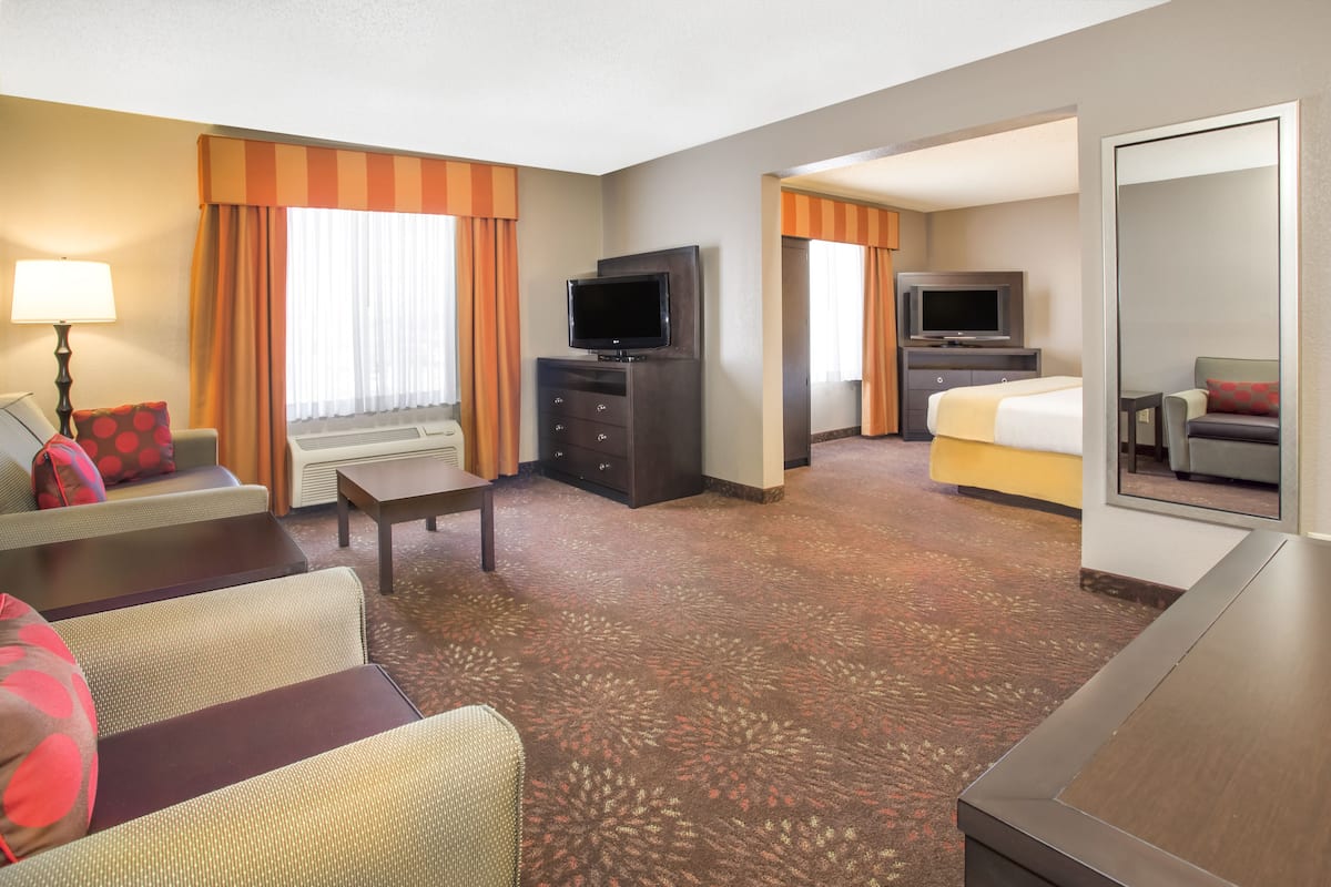 Habitación de hotel con sofá, televisión, cama, escritorio y espejo.