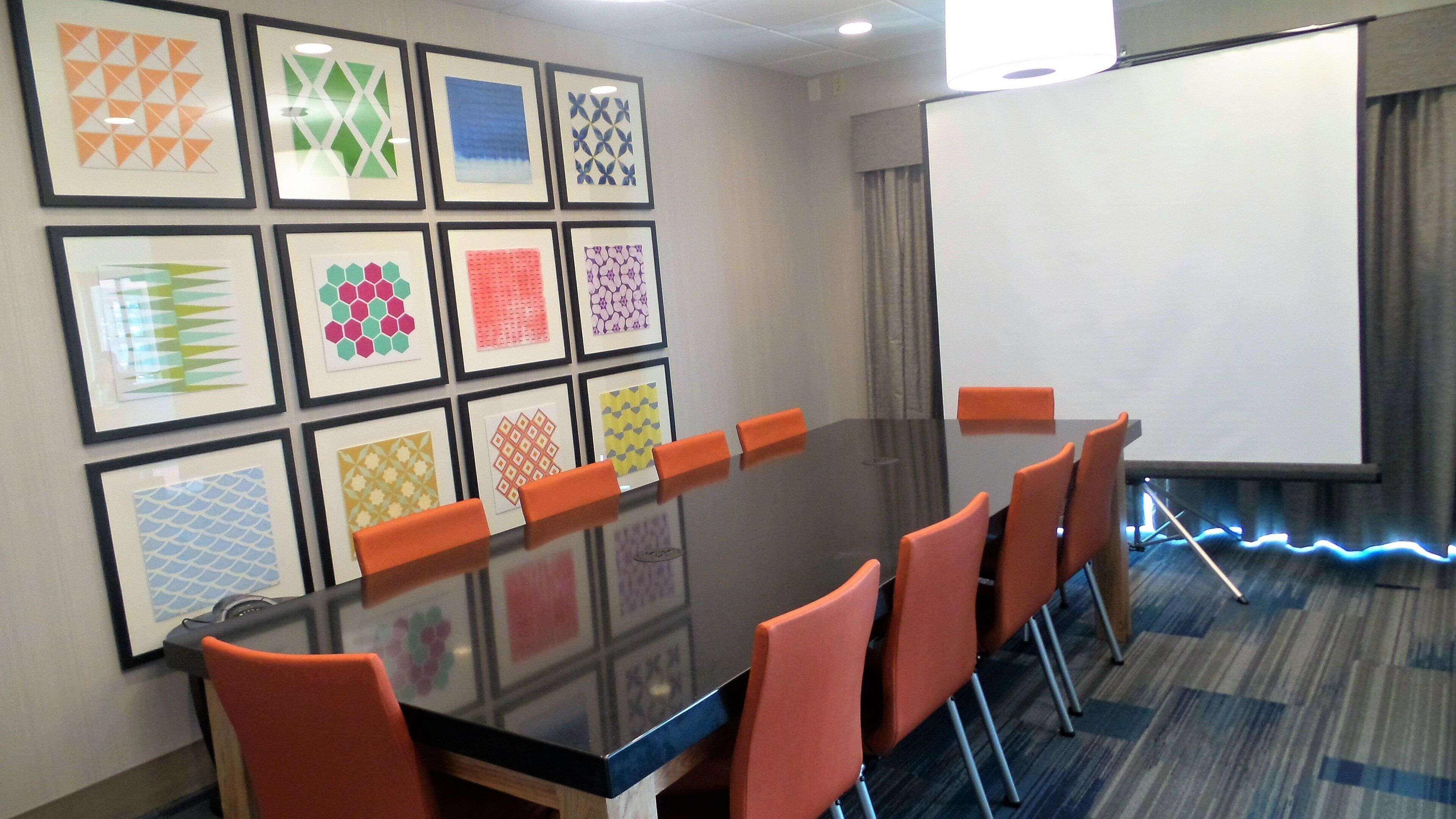 A conference room with a long table, orange chairs, and a projector screen.