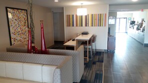 A hotel lobby with a seating area, a reception desk, and a corridor leading to other rooms. - Muncie Place Hotel & Suites (Muncie)