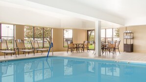 Une piscine intérieure dotée de chaises longues et de tables, de grandes fenêtres et offrant une vue sur l’extérieur.