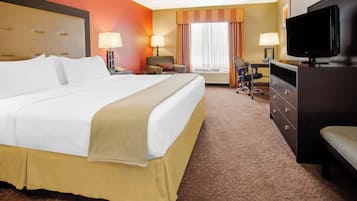 A hotel room with a large bed, two chairs, a desk, a television, and a dresser.