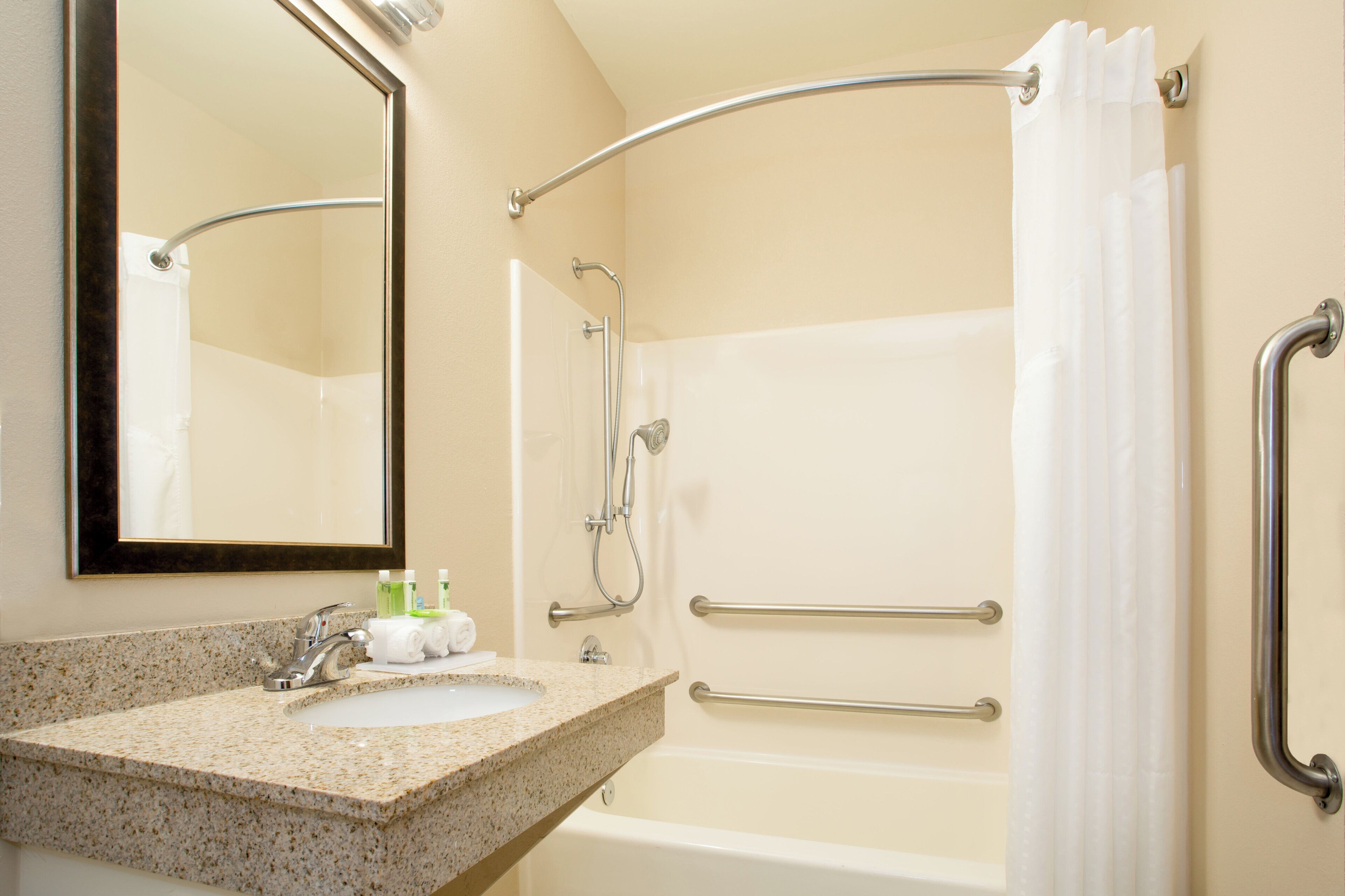 A bathroom with a granite countertop, a sink, a mirror, a shower with a grab bar, and a bathtub.