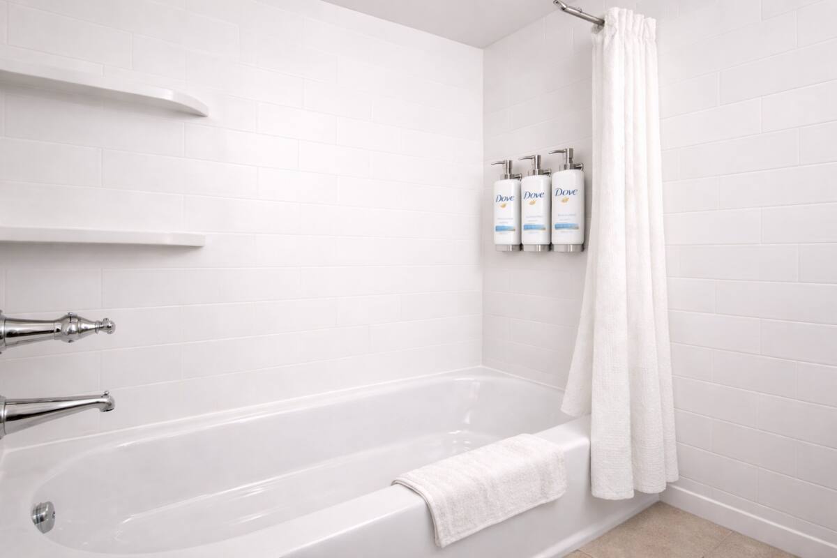 Ein modernes Badezimmer mit einer weißen Badewanne, Chromarmaturen und Dove-Toilettenartikeln auf einem Wandregal.