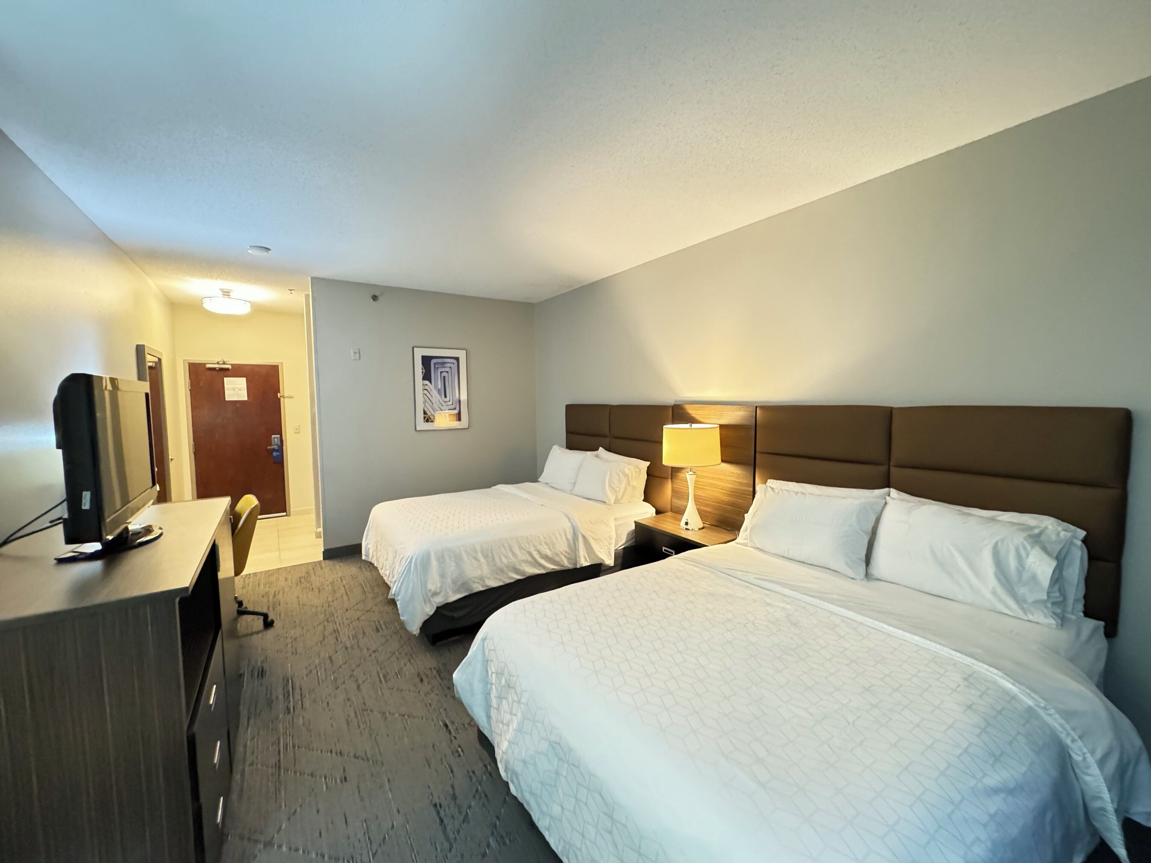 A hotel room with two beds, a desk, a television, and a door.