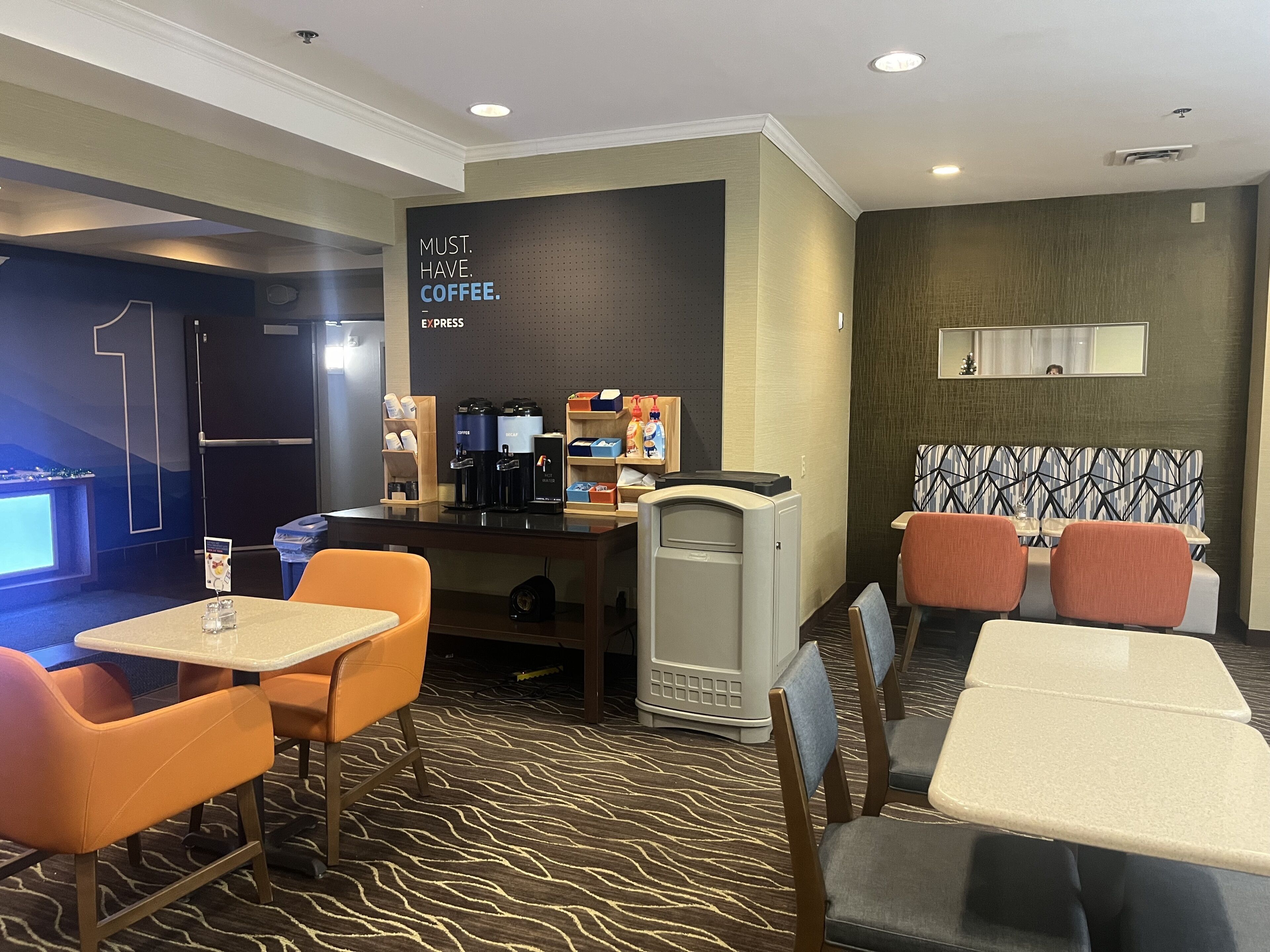 A hotel room with a coffee station, seating area, and a wall with a motivational quote.