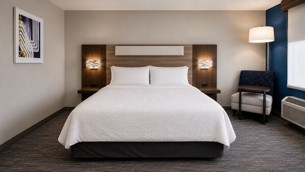 Ein Hotelzimmer mit einem großen Bett, zwei Nachttischen mit Lampen, einem kleinen Beistelltisch, einem Sessel und einem Wandbild.
