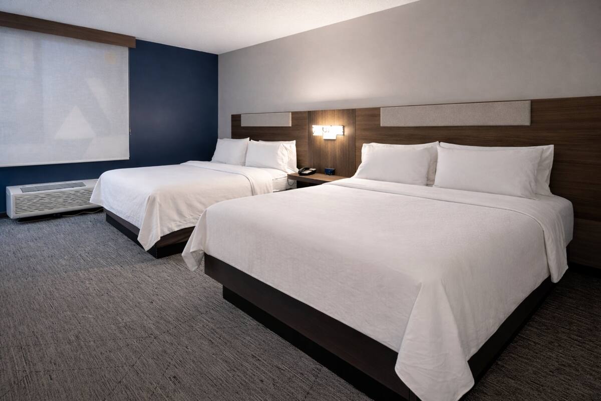Ein Hotelzimmer mit zwei Betten, einem Wandheizkörper und einem großen Fenster mit Jalousien.