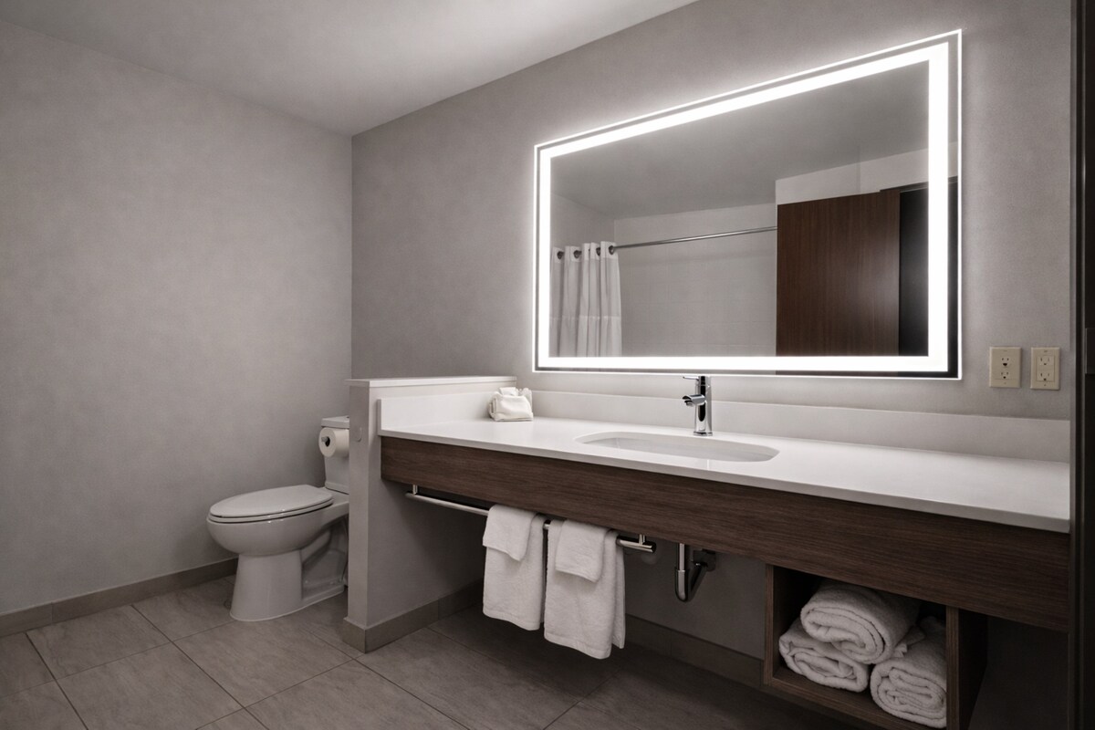 Une salle de bain moderne avec un lavabo blanc, un grand miroir doté d’un éclairage à LED, des toilettes et un porte-serviettes avec des serviettes.