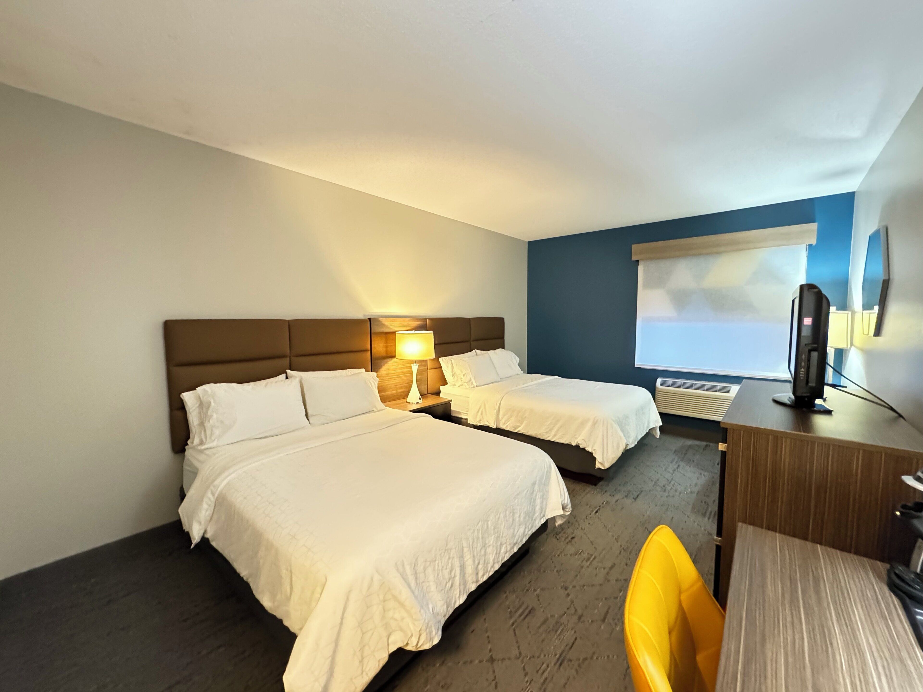 Quarto de hotel com duas camas, uma escrivaninha, uma cadeira, uma televisão e uma janela.