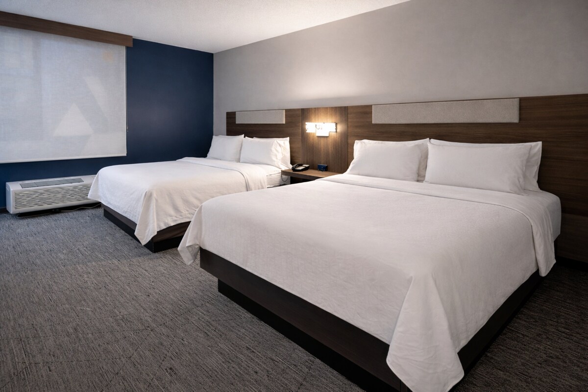 Une chambre d’hôtel avec deux lits, un radiateur fixé au mur et une grande fenêtre avec des stores.