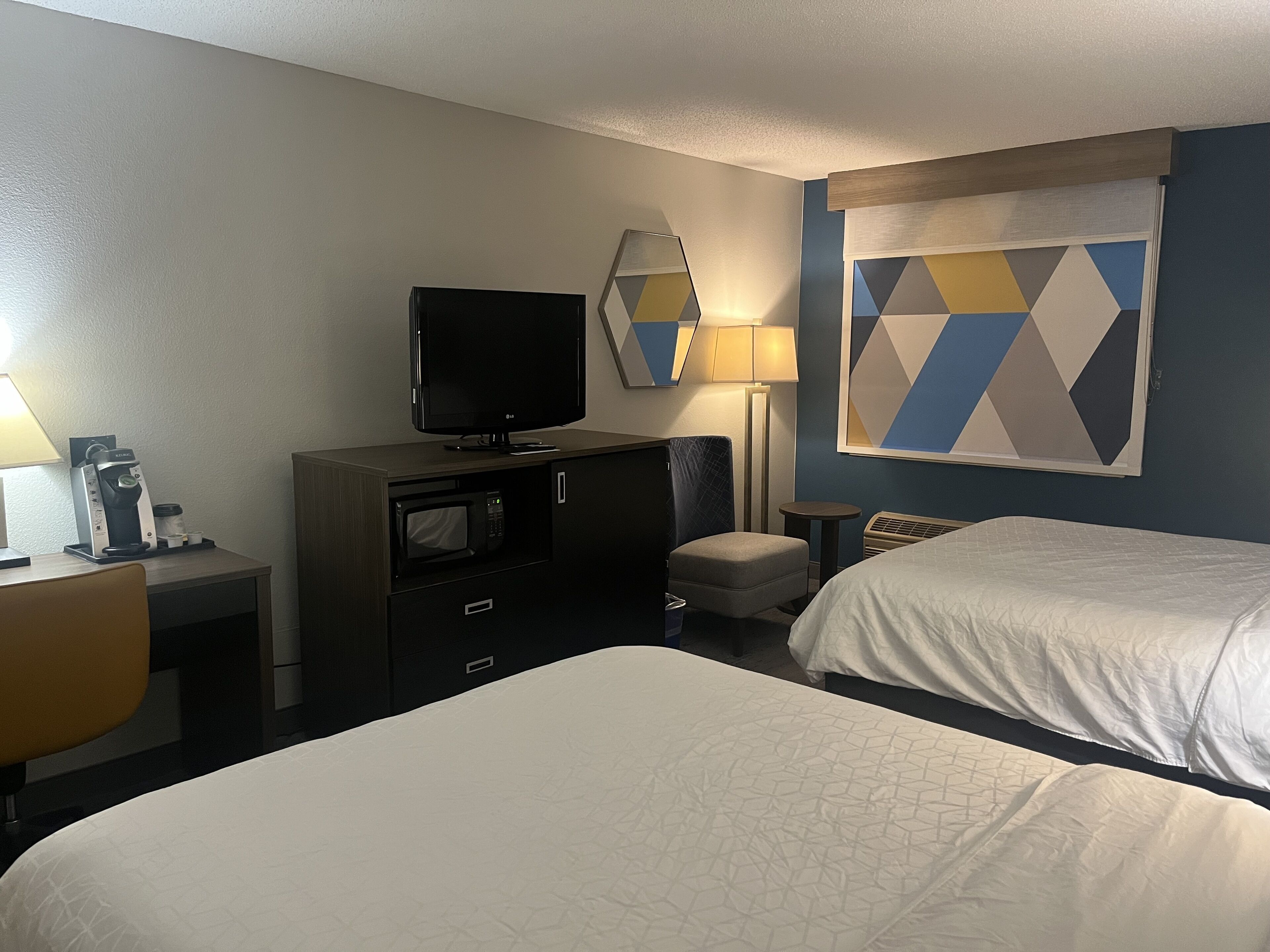A hotel room with a bed, a desk with a coffee maker, a television, a microwave, and a small table.