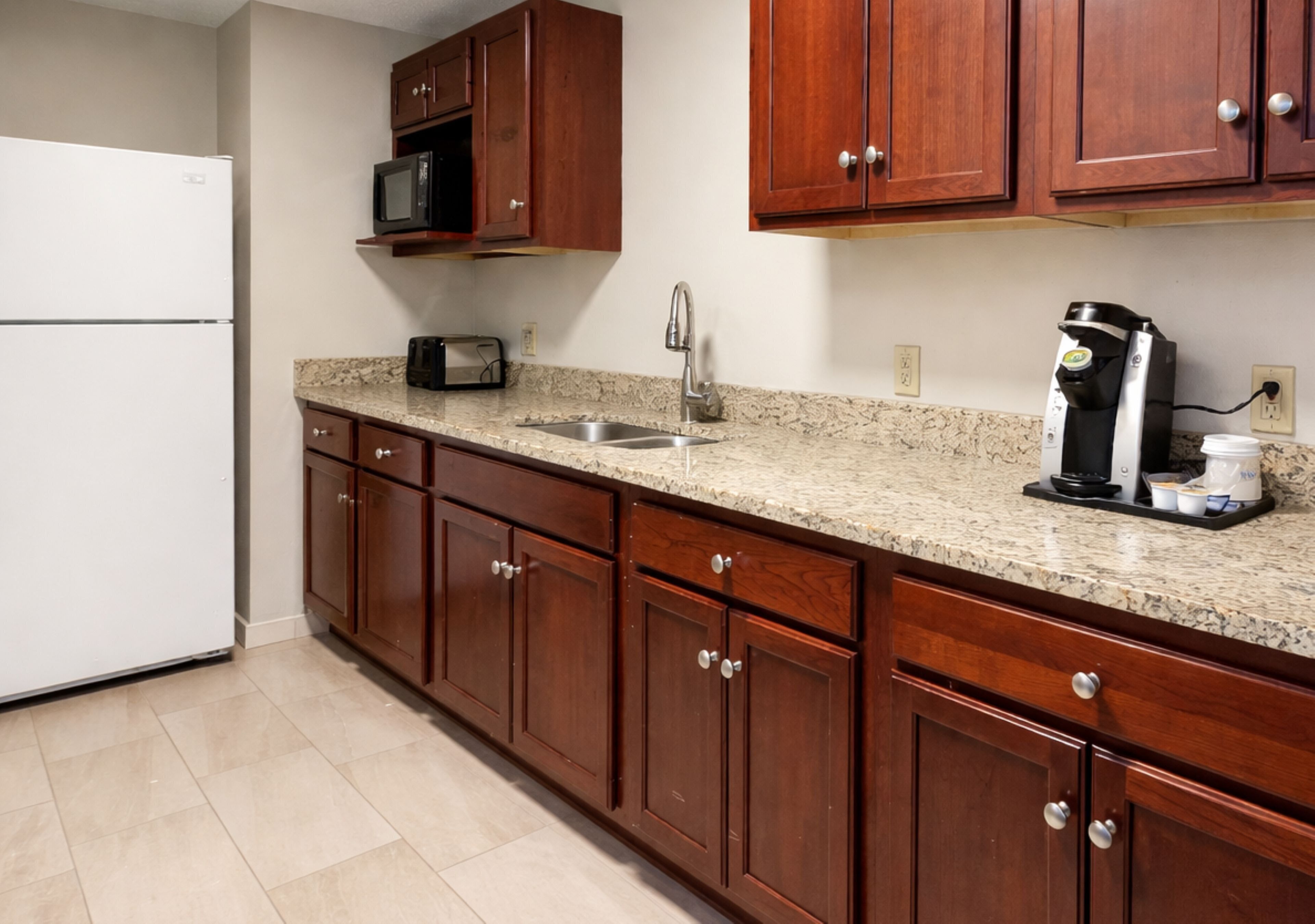 A kitchen with wooden cabinets, a white refrigerator, a microwave, a toaster, a coffee maker, and a sink.