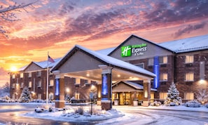 Ein Holiday Inn Express & Suites Gebäude mit überdachter Einfahrt, Backsteinfassade und verschneiter Umgebung.