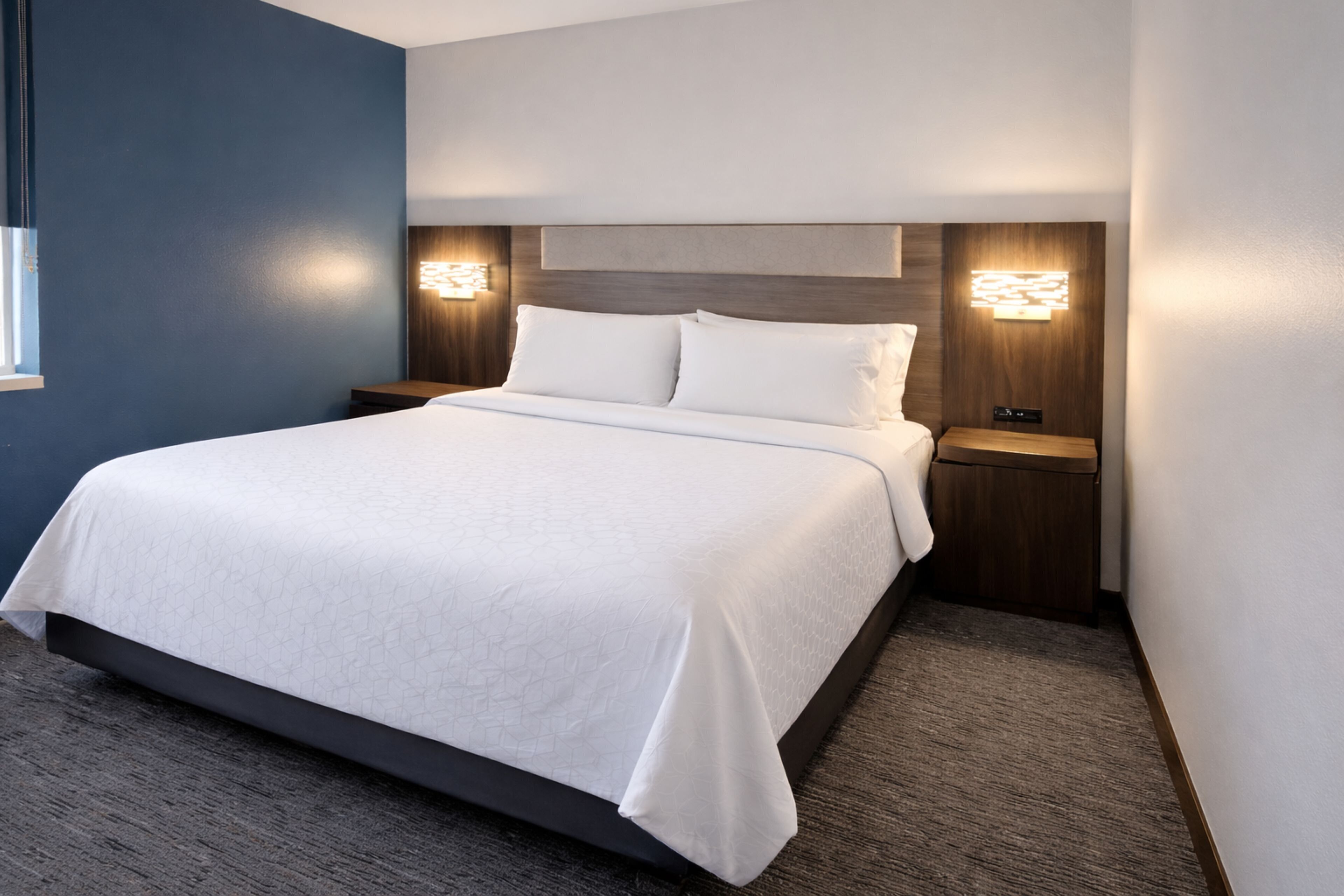 Una habitación de hotel moderna con una cama grande, dos mesitas de noche e iluminación empotrada.