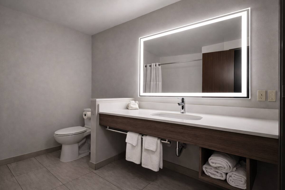 Ein modernes Badezimmer mit einem weißen Waschbecken, einem großen Spiegel mit LED-Beleuchtung, einer Toilette und einem Handtuchhalter mit Handtüchern.