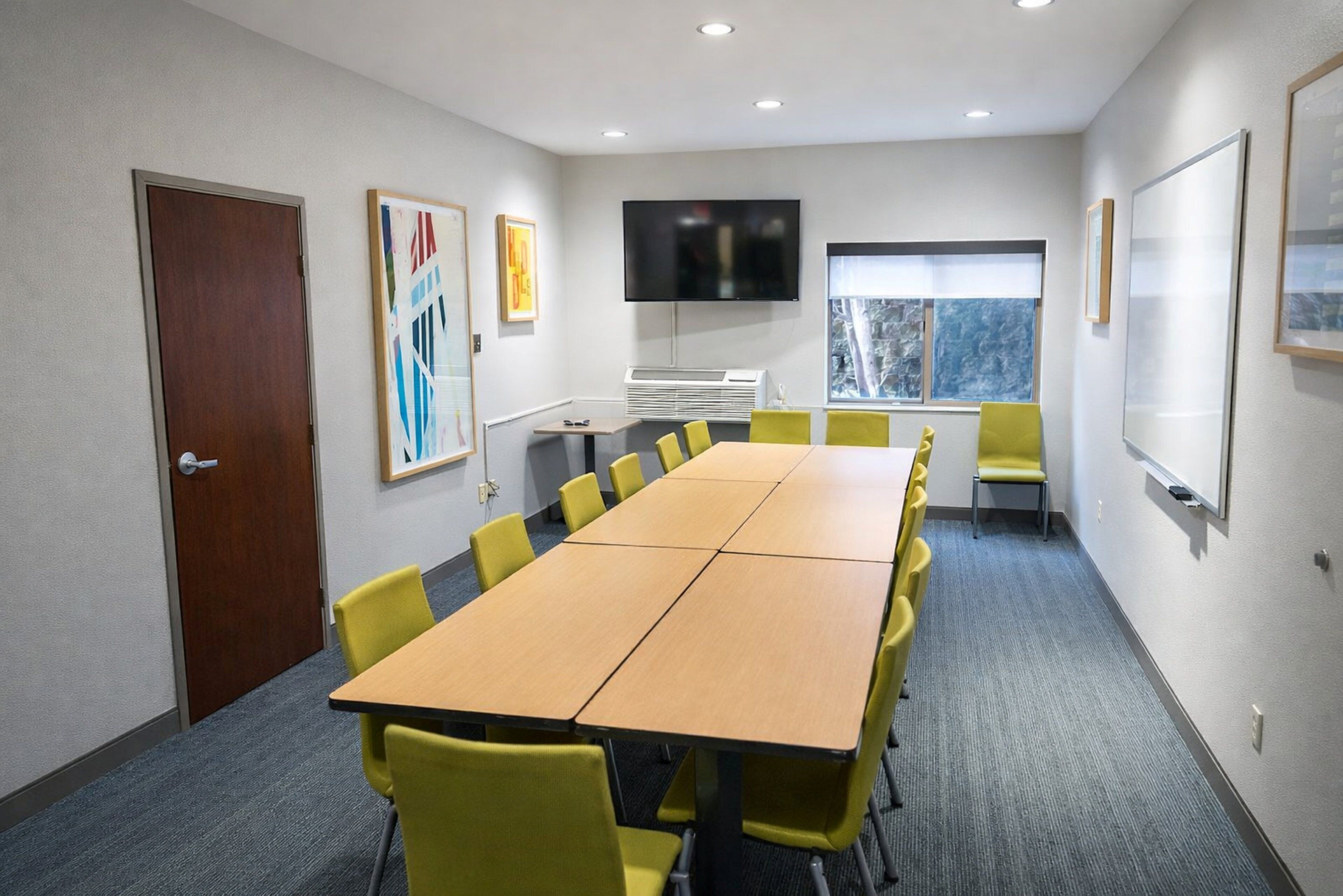 A conference room with a long table, yellow chairs, a flat-screen TV, and framed artwork on the walls.