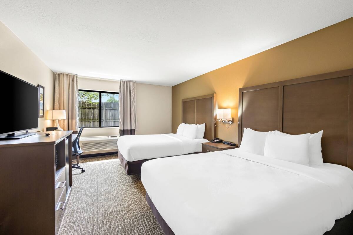 A hotel room with two beds, a desk with a TV, a chair, and a window with curtains.