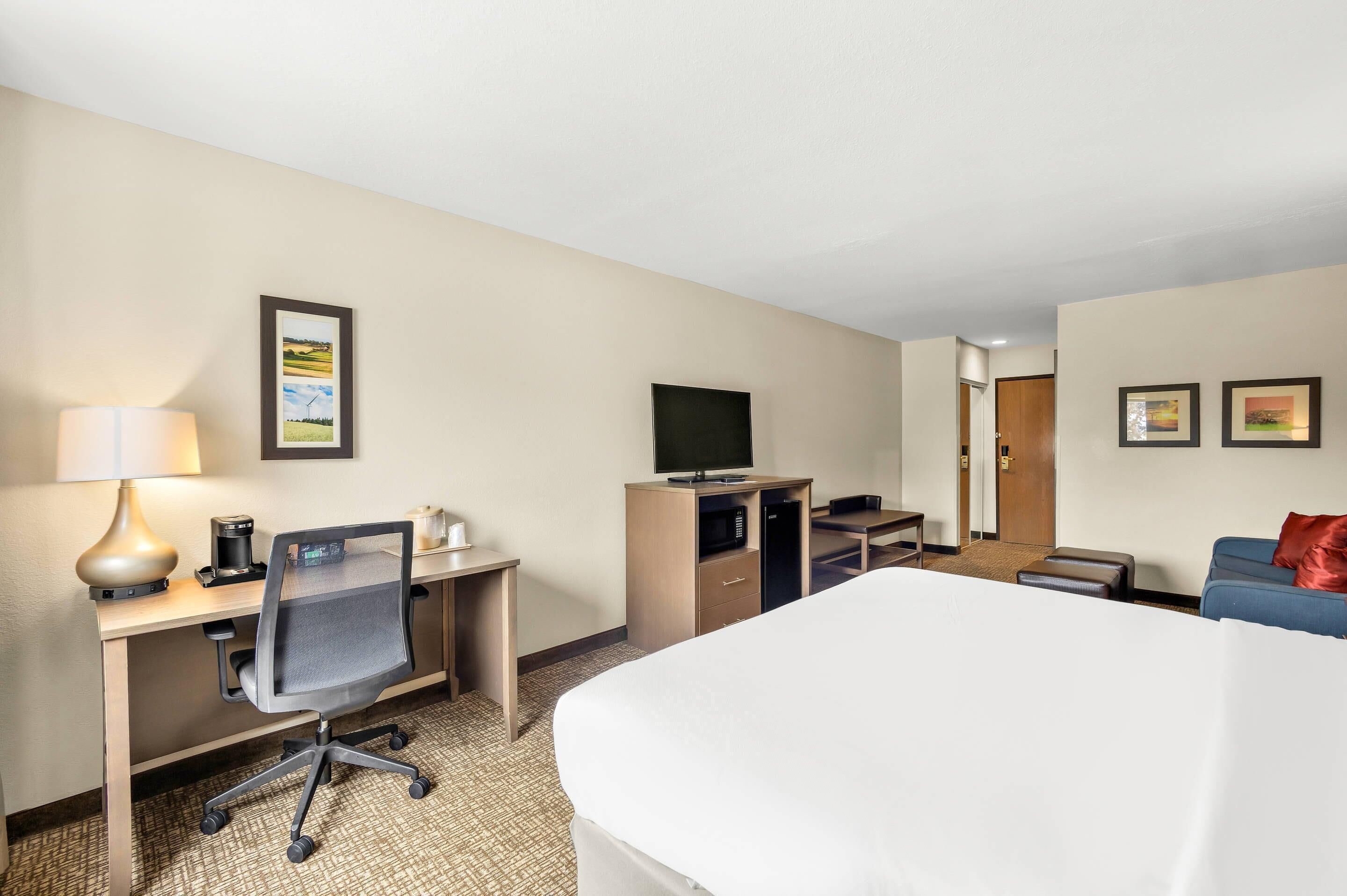Een hotelkamer met een bed, bureau, stoel, televisie en een zithoek met een bank en poef.
